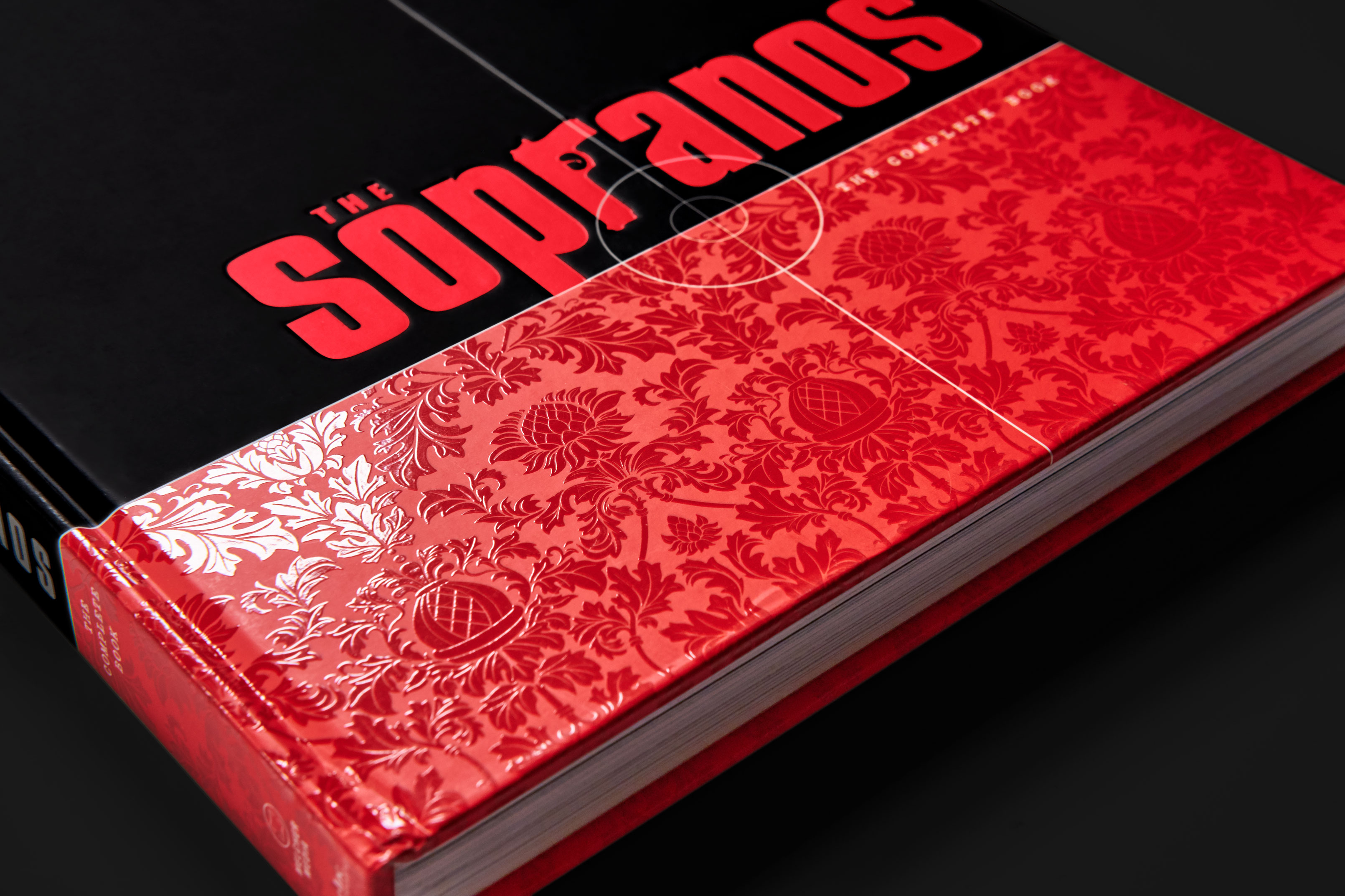 Closeup of botanical wallpaper pattern printed in gloss atop red color on cover.